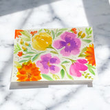 Hand-painted 5x7-inch greeting card featuring bold, layered watercolor florals in orange, yellow, pink, and purple on textured paper, with matching motifs on the envelope and inside.