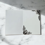 Hand-painted 5x7-inch greeting card featuring layered black watercolor florals on textured white paper, with matching painted motifs on the envelope and interior.