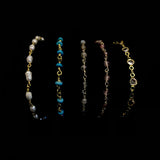 Image of 5, 14k yellow gold plated bracelets in front of a black background. From left to right the bracelets are made of freshwater pearl, turquoise, labradorite, strawberry quart and clear crystal