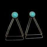 Image of faceted turquoise earrings with two, thin gold plated, overlapping triangles underneath, on a black background.